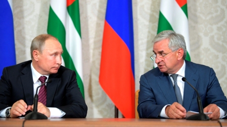 Bildet viser Russlands president Vladimir Putin og tidligere leder for Abkhazia, Raul Khadzhimba, i samtale foran sine respektive flagg i 2017